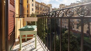 A balcony with a green cushion and a small table, overlooking a cityscape with multiple buildings.