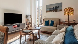 A living room with a flat-screen TV, a bookshelf, a patterned sofa, a coffee table, and a decorative lamp.