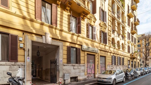 A yellow building with a sign reading "ARREDAMENTI" and a row of parked cars on the street.