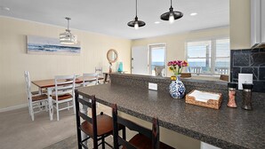 A kitchen with a granite countertop, white chairs, a vase with flowers, and pendant lights. - 3 Bed/2 Bath Boardwalk Oceanfront at Ocean Beach (Ocean City)