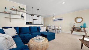 A living room with a blue sofa, a round woven coffee table, and a dining area with white chairs and a wooden table. - 3 Bed/2 Bath Boardwalk Oceanfront at Ocean Beach (Ocean City)