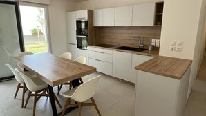 A modern kitchen with white cabinets, a wooden countertop, and a dining area with a table and chairs. - Cocon Neuf 6/8 pers à 2 pas des Plages, Port & Centre Ville (Saint-Pierre-Quiberon)