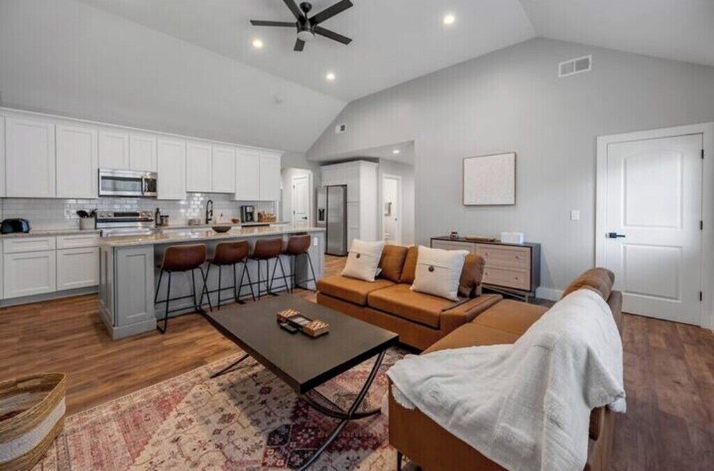 Una cocina moderna con armarios blancos, una isla central con taburetes y un sofá marrón junto a una silla blanca.
