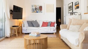 A modern living room with a white sofa, a round wooden coffee table, and a television mounted on the wall. - Ro-ana for 6, Gerringong (Gerringong)