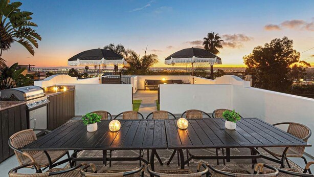 An outdoor dining area with a grill, wicker chairs, and a view of the sunset.