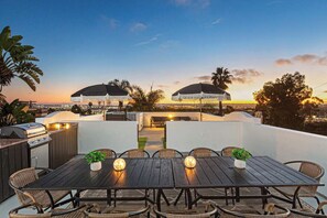An outdoor dining area with a grill, wicker chairs, and a view of the sunset.