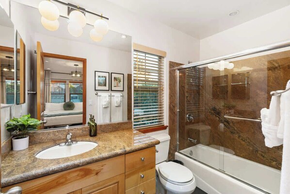 A modern bathroom with a granite countertop, a white sink, a glass-enclosed shower, and a large mirror.