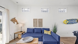 A living room with a blue sofa, a wooden coffee table, a lamp, and a wall-mounted surfboard. - Game Room, Dogs Ok, Walk to Beach (Breakaway) (Ocean Park)