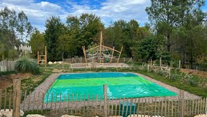 A fenced outdoor area with a pool, wooden play structures, and surrounding trees. - STOERbuiten Les Charmes (Saint-Andre-d'Allas)