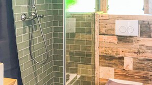 Suihkukaappi lasiovella, wc, jossa on pyyhe, ja ikkuna, josta avautuu näkymä vehreään maisemaan.