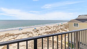 Blick auf einen Strand vom Balkon aus, mit einem Haus im Vordergrund.