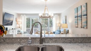 A kitchen with a double sink, a chandelier, and a view of the outdoors. - Beachwalk 105, Oceanfront Condo in Pine Knoll Shores, NC! (Pine Knoll Shores)