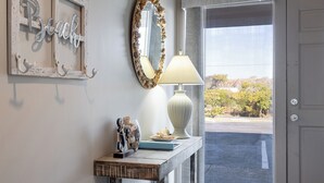 A hallway with a decorative mirror, a lamp, and a small table with a vase and figurines. - Beachwalk 105, Oceanfront Condo in Pine Knoll Shores, NC! (Pine Knoll Shores)