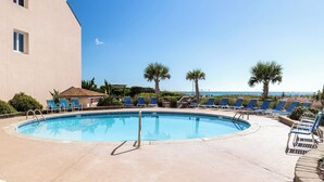 A pool area with lounge chairs and palm trees, overlooking a body of water. - Beachwalk 106, Oceanfront Condo in Pine Knoll Shores, NC! (Pine Knoll Shores)