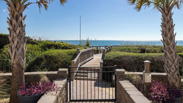 A wooden boardwalk leading to a beach with palm trees and a clear sky. - Beachwalk 106, Oceanfront Condo in Pine Knoll Shores, NC! (Pine Knoll Shores)
