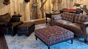 Una habitación rústica con paredes de madera, adornos de animales colgados, un candelabro, mobiliario de cuero y una alfombra estampada.