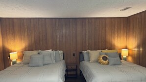 Una habitación con dos camas, paneles de madera en las paredes y lámparas de noche.