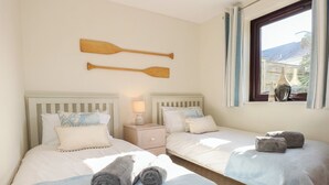 A twin room with two beds, each with a pillow, a nightstand, and a lamp. There are two wooden paddles on the wall above the beds. - Hafan Bach - 233 Cae Du (Pwllheli)