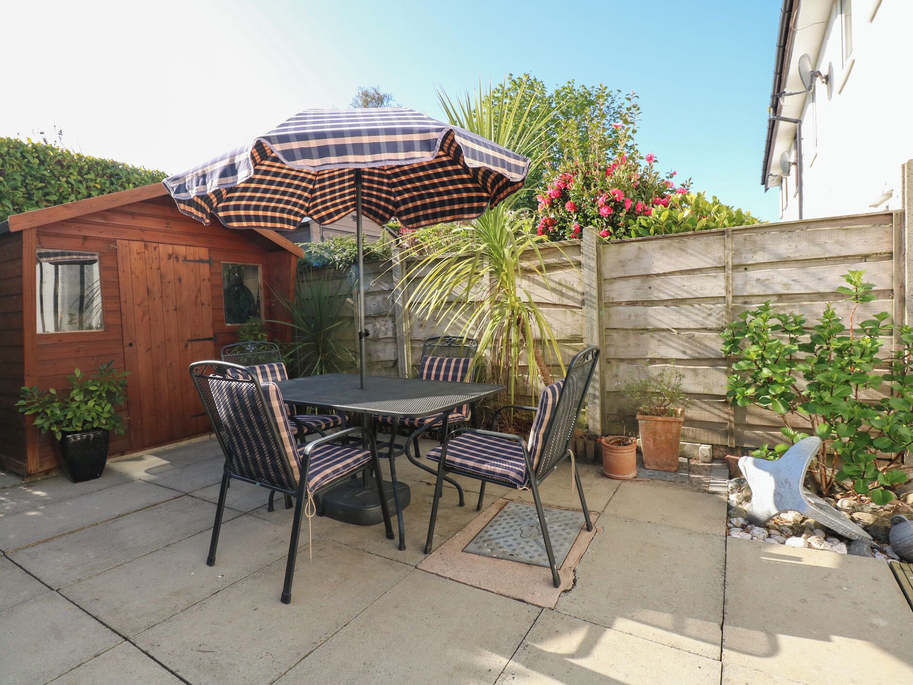 An outdoor patio with a table and chairs, a checkered umbrella, and potted plants.
