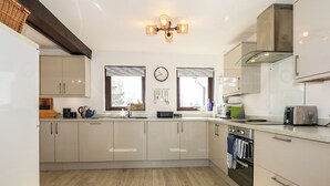 A modern kitchen with light-colored cabinets, a stainless steel range hood, and a window with a view of the outdoors. - Hafan Bach - 233 Cae Du (Pwllheli)