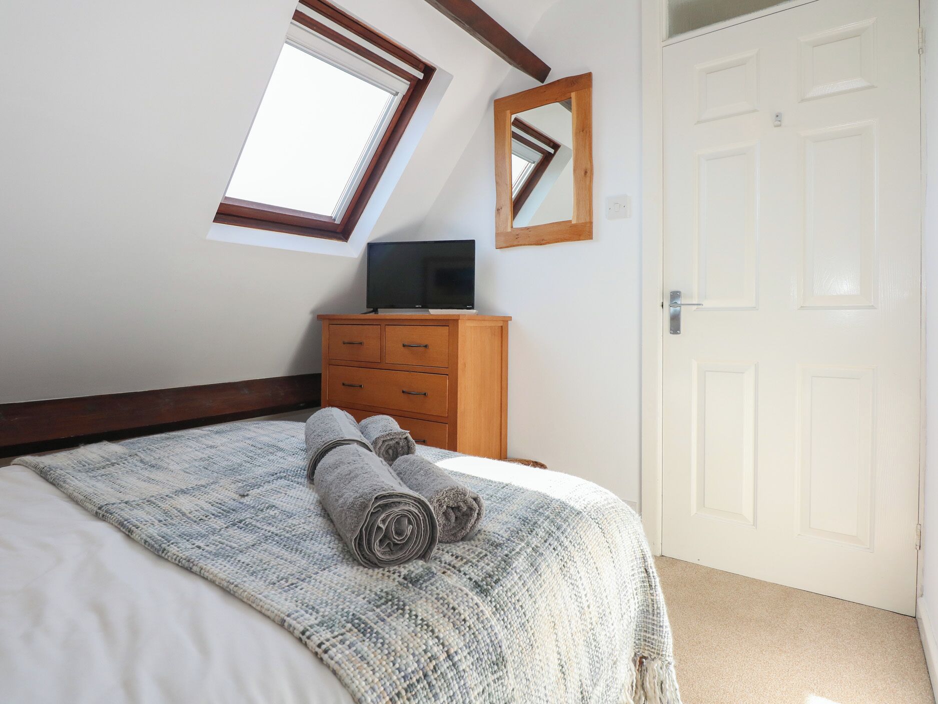 A bedroom with a bed, a wooden dresser, a television, a window, and a door.