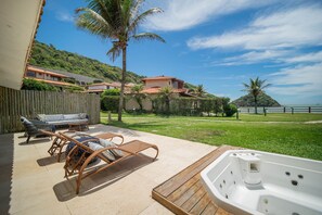 Un patio con mobiliario de mimbre y un jacuzzi, con vistas a una colina con casas y al mar.