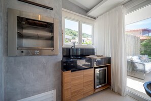 Cocina moderna con horno integrado, un lavamanos y ventana con vistas a un balcón.