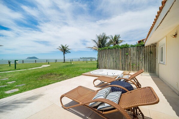 Un patio con mobiliario de mimbre y un jacuzzi, con vistas a una playa y el océano.