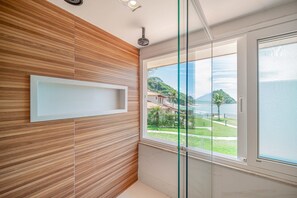 Un baño moderno con un panel de madera en la pared, cabina de ducha de vidrio y vistas a un paisaje costero.