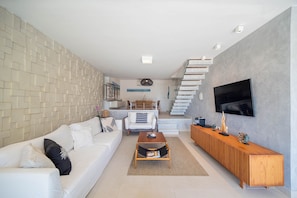 Una sala de estar moderna con un sofá blanco, una mesa de centro de madera y un televisor montado en la pared.