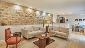 Ein Wohnzimmer mit Steingemäuer, zwei Sofas, einem Holztisch und einem Essbereich mit Stühlen und Tisch.