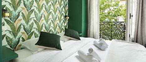 A hotel room with a bed, pillows, a window with a view of buildings, and a green wall with a leaf pattern.