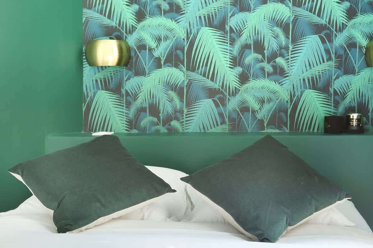 Ein Schlafzimmer mit grüner Wand, strukturiertem Wandpapier und zwei dunklen Kissen auf einem Bett.