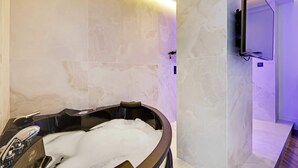 A modern bathroom with a freestanding bathtub, marble walls, and a mounted television.
