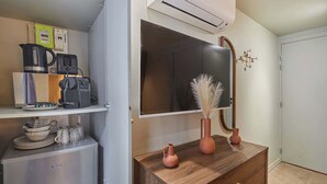 A kitchenette with a coffee maker, a microwave, and a small refrigerator. There is a wooden dresser with two vases and a mirror. An air conditioning unit is mounted above the mirror.