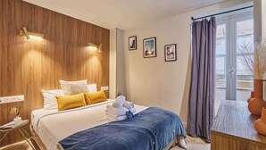 A hotel room with a bed, bedside table, wall-mounted light, window with curtains, and framed pictures.