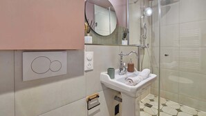 A modern bathroom with a glass shower enclosure, a sink with a mirror, and a wall-mounted light fixture.