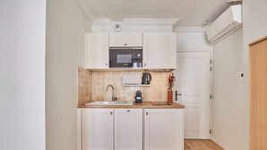 Une cuisine compacte avec des meubles blancs, un four à micro-ondes, une machine à café et un évier.