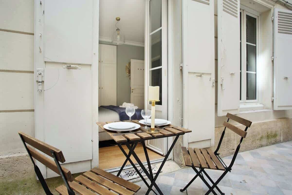 Un petit espace de vie à aire ouverte, avec une table en bois dressée pour deux personnes, un banc et une porte donnant sur une chambre.