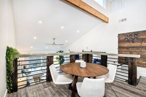 A modern dining area with a round wooden table and white chairs, a ceiling fan, and a view of a balcony with plants. - Sea Bluff - Direct Beach Access (Encinitas)