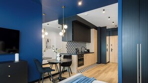 Ein modernes Hotelzimmer mit Bett, Schreibtisch, Stuhl, Fernseher, Küchenzeile und Bad.