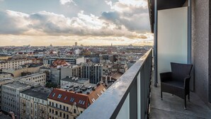 Ein Balkon mit Blick auf einen Stadtblick, darunter verschiedene Gebäude und ein weiter Turm in der Ferne.