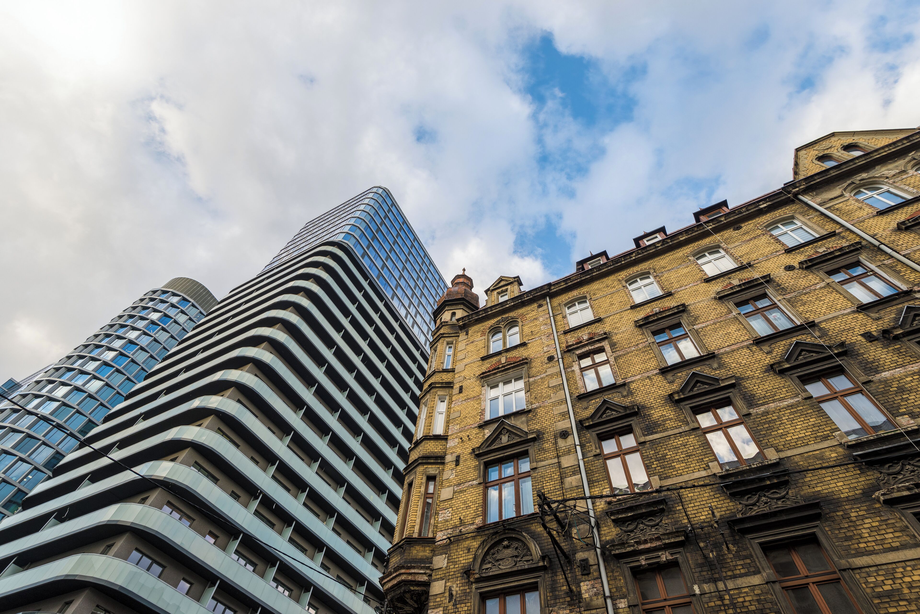 A modern high-rise building with a curved facade and a traditional brick building with multiple windows and a corner turret.