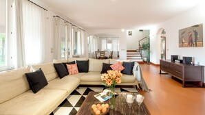 A spacious living room with a beige sectional sofa, a coffee table with oranges and a vase of flowers, and a staircase leading to an upper floor. - La Scuderia 8, Emma Villas (Savignano Sul Rubicone)