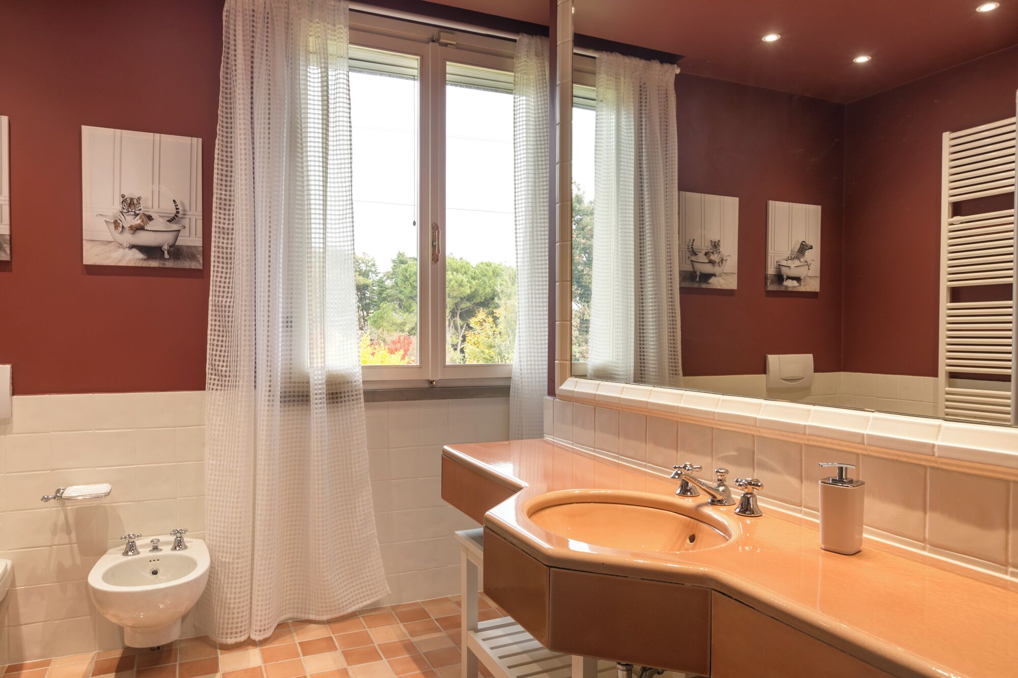 A bathroom with a beige sink, a bidet, and a window with a view of trees.