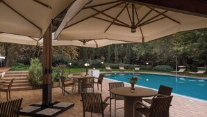 An outdoor pool area with lounge chairs, a table, and umbrellas providing shade. - La Scuderia 8, Emma Villas (Savignano Sul Rubicone)