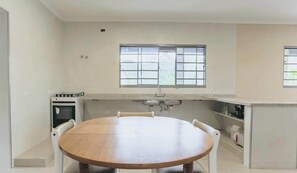A kitchen with a round wooden table, a stove, and a window above the sink. - Casa  em Parelheiros com Piscina e Churrasqueira (São Paulo)