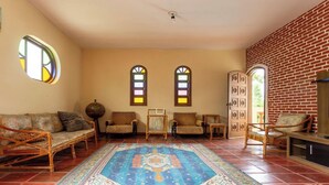 Una habitación de diseño tradicional con un sofá de ratán, sillas estampadas, un tapete azul con motivos y dos ventanas con vitrales.