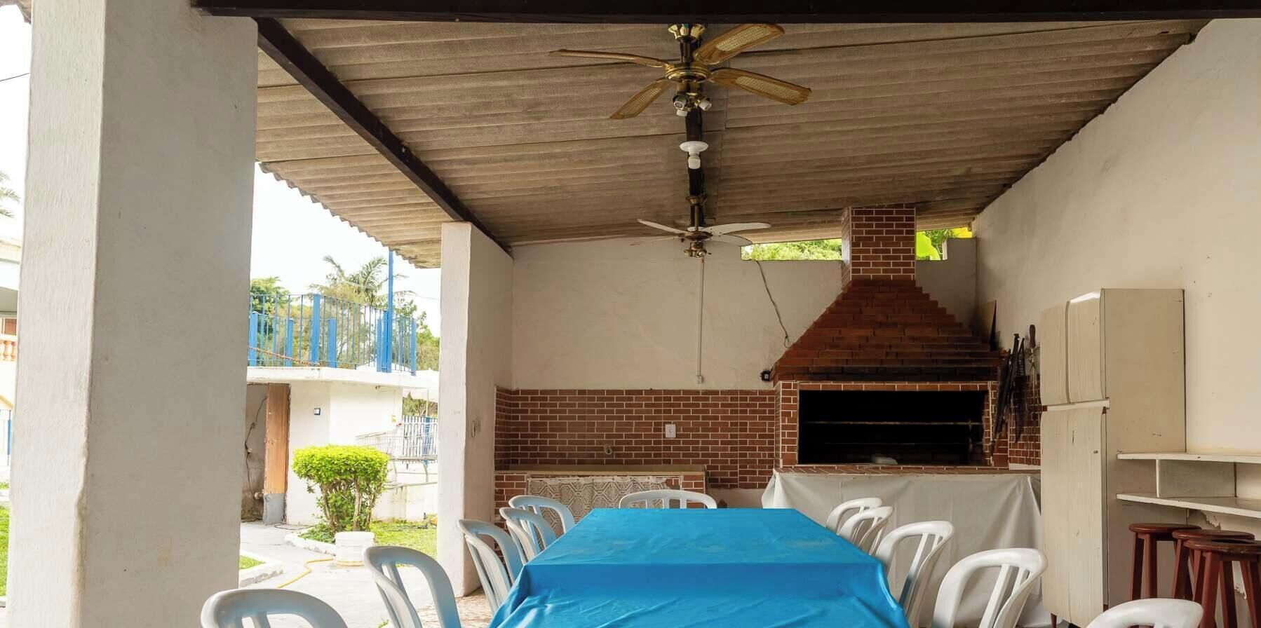 Un patio al aire libre con un horno de ladrillo, sillas de plástico blanco y un mantel azul.