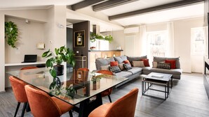 Una sala de estar moderna con una mesa de comedor de vidrio, sillas naranjas, un sofá gris con cojines estampados y una mesa de centro.
